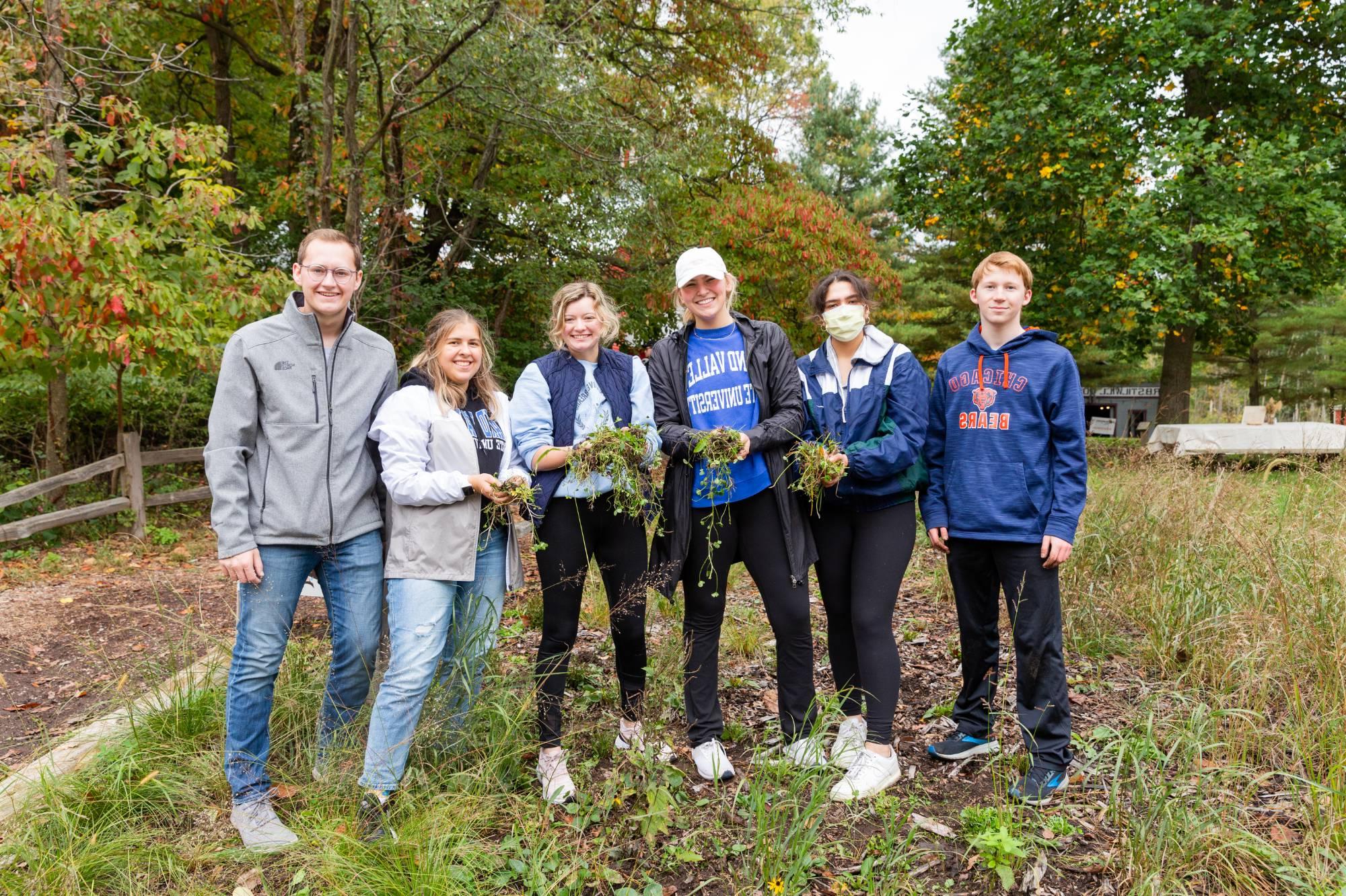 Students holding gardening tools while volunteering